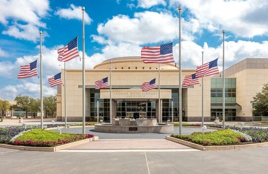 Exterior of the George W. Bush Presidential Museum in Dallas, Texas, featuring stately architecture, large windows, and a landscaped entrance area.