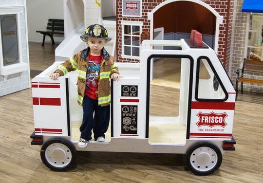 Young child sitting in a toy vehicle at Play Street Museum - Plano, enjoying interactive play in a kid-friendly museum setting.