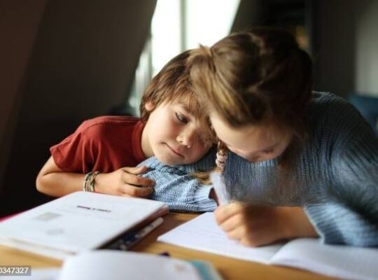 Two children engaged in creating art, focused on their drawings with colorful supplies scattered around them, showcasing creativity and imagination.