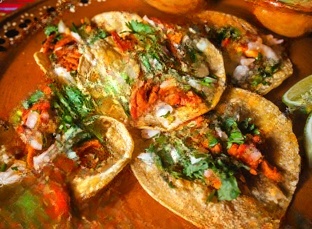 A vibrant platter showcasing carne asada, al pastor, and barbacoa tacos, garnished with fresh cilantro, diced onions, and lime wedges, served with salsa on the side.