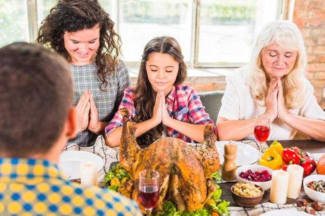 Family members praying before thanksgiving dinner one of Thanksgiving and Christmas traditions.