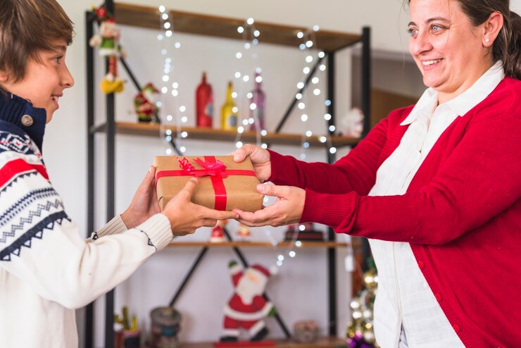 Woman offering gift to a child a Decorating the Christmas tree is a beloved tradition that brings families together. Everyone hangs ornaments, strings lights, and adds their special touch. It’s a joyful, memorable way to celebrate the holiday season and create lasting memories. Enjoy the magic of decorating this year. Gift Giving and Stocking Stuffers: 