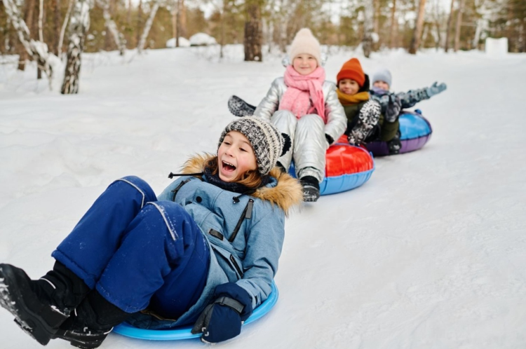 Children sledding and sliding down a snowy hill on colorful snow tubes in a winter forest,.