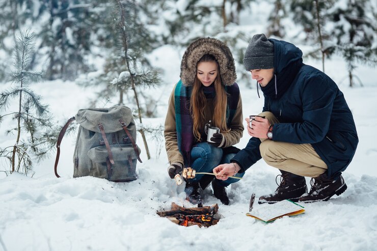 A couple starting a campfire in a snowy forest during a winter outdoor adventure.