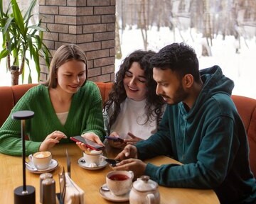 Three young friends sitting at a table in a café, looking at their phones and engaged in conversation, one of the activity from the Dallas winter bucket.