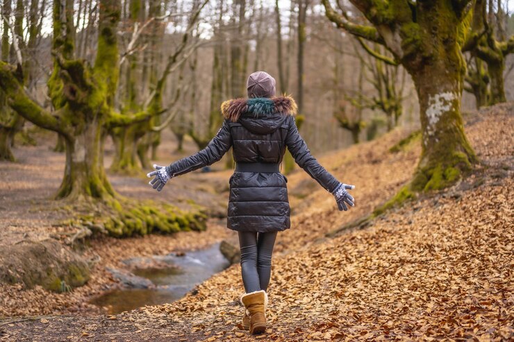 A person dressed in warm winter clothing walking down a forest path covered in fallen leaves, one of the activity from the Dallas winter bucket.